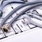 Close-up of plumbing tools and faucet on top of an architectural blueprint, perfect for hardware and construction themes.