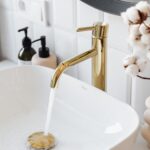 A stylish bathroom sink with a modern gold faucet and running water for a touch of luxury.