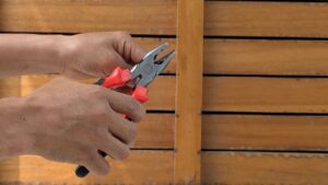 A detailed view of hands holding red pliers against a wooden backdrop, depicting a DIY or repair scene.
