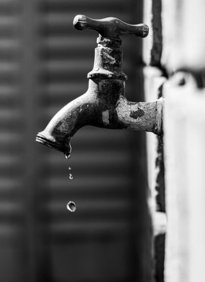 Black and white photo of a vintage water tap dripping water drops with a blurred background